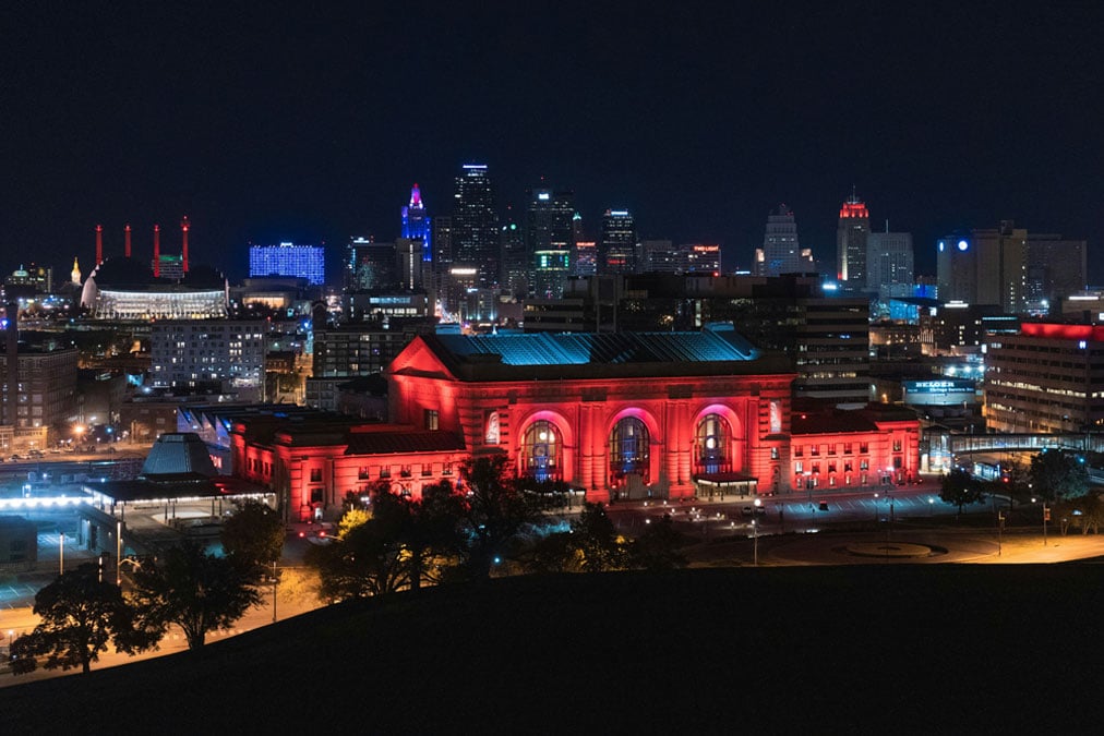 kansas-city-skyline-night Kansas City skyline at night with an illuminated Union Station building in the foreground, glowing red, surrounded by other lit-up structures.