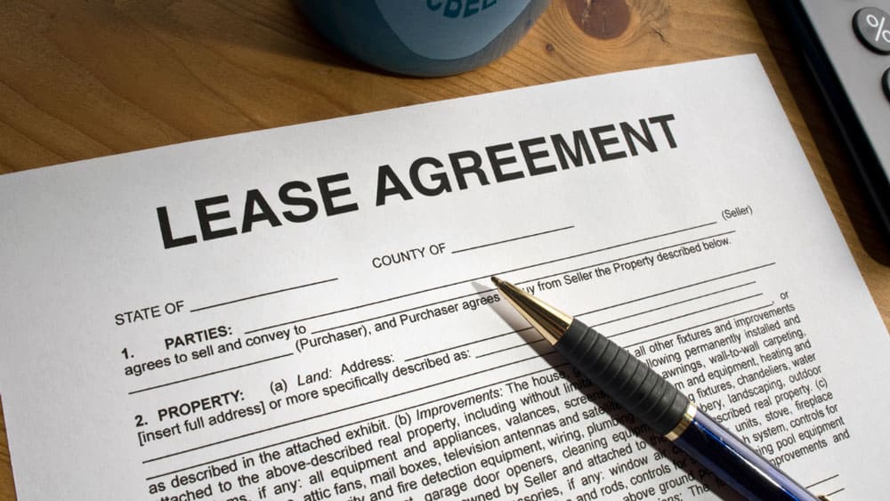 lease-agreement-on-desk A lease agreement form with a pen on a wooden table, partially visible, with a blue mug in the background.